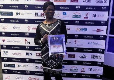 Rosaline holder her certificate in front of a logo board