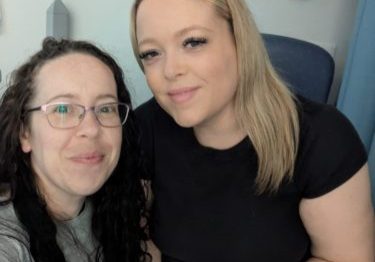 Rebecca, crouched down next to Holly who is sitting on a chair.
