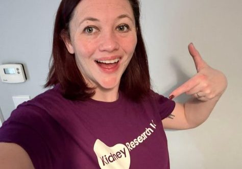 Beck, wearing her purple t-shirt and pointing at the logo