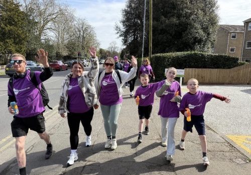 Group of adults and children, all wearing purple Kidney Research UK t-shirts, doing the March March