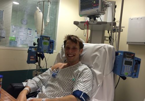 Jonny, in a hospital bed with monitoring machines next to him