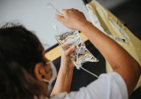 Female nurse with back to camer, wearing a mask, hanging up a fluids bag.