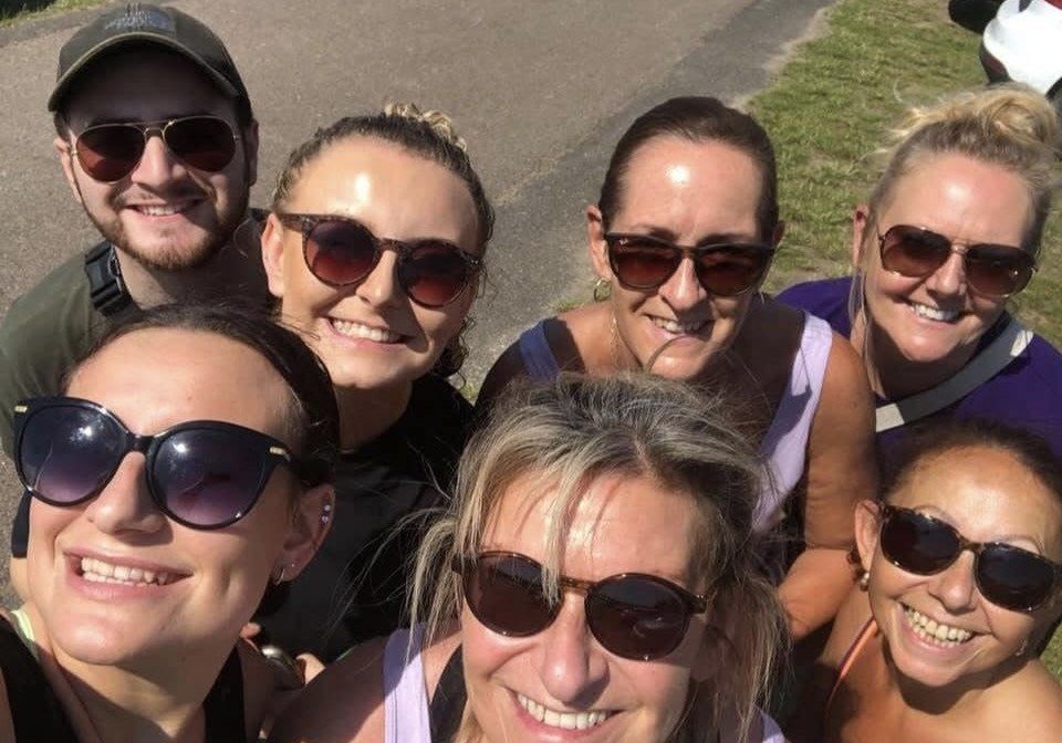 A group of seven friends, all taking a selfie looking up to the camera