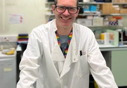 Matt, wearing a white lab coat, standing behind a lab bench.