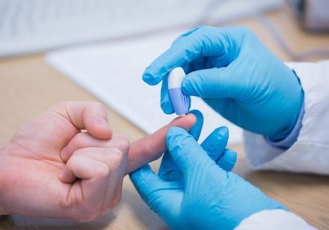 Hands of a medical person, wearing blue latex gloves, doing a finger prick test on a patient.