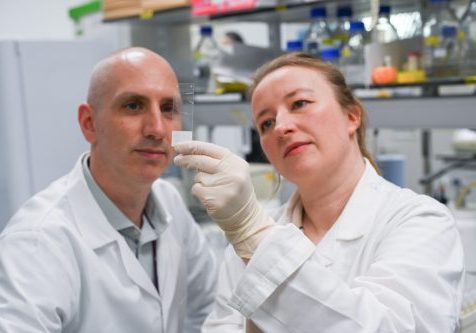 Simon Baker and Jenny Hinley in the lab, holding up a microscope slide